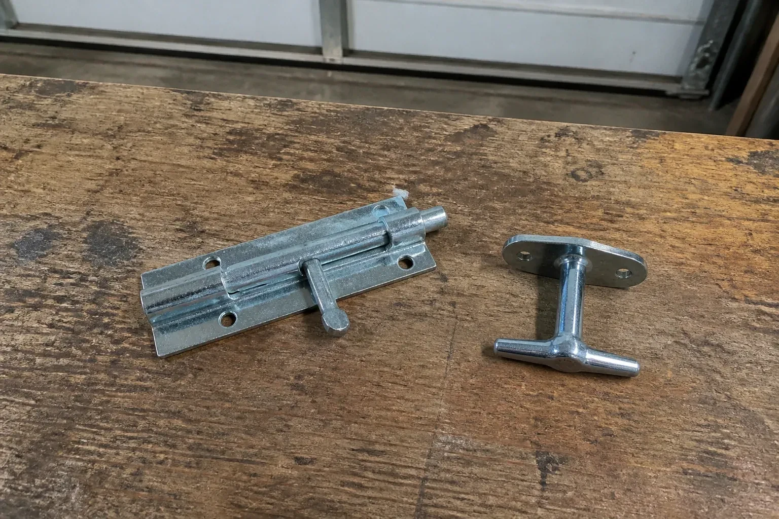 Detached slide bolt and T-handle on a wooden garage workbench. — Garage Door Manual Lock Repair, Kitchener