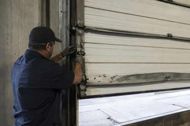Person holding tools at the side hinge of a partly raised industrial sectional door — Commercial Sectional Door Repair, Kitchener
